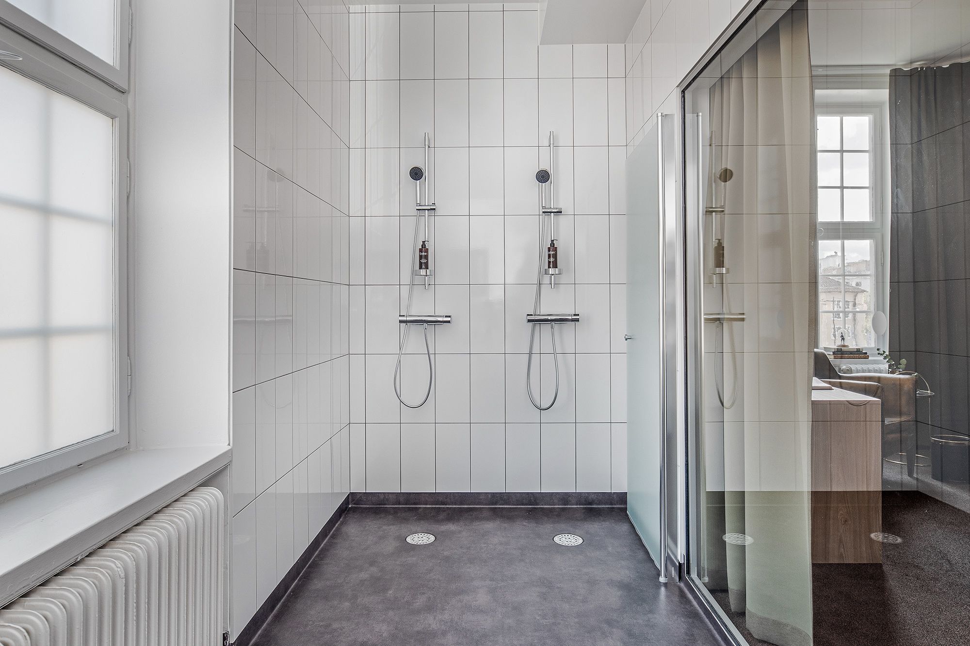 Une salle de bain moderne avec une douche à l’italienne en verre, des murs recouverts de carreaux blancs et un sol foncé.