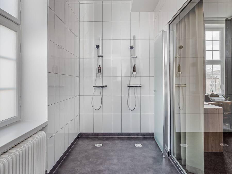 Une salle de bain moderne avec une douche à l’italienne en verre, des murs recouverts de carreaux blancs et un sol foncé.