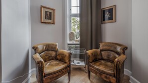 Ein Zimmer mit zwei Ledersesseln, einem Heizkörper, einem Fenster mit Vorhängen und gerahmten Bildern an den Wänden.