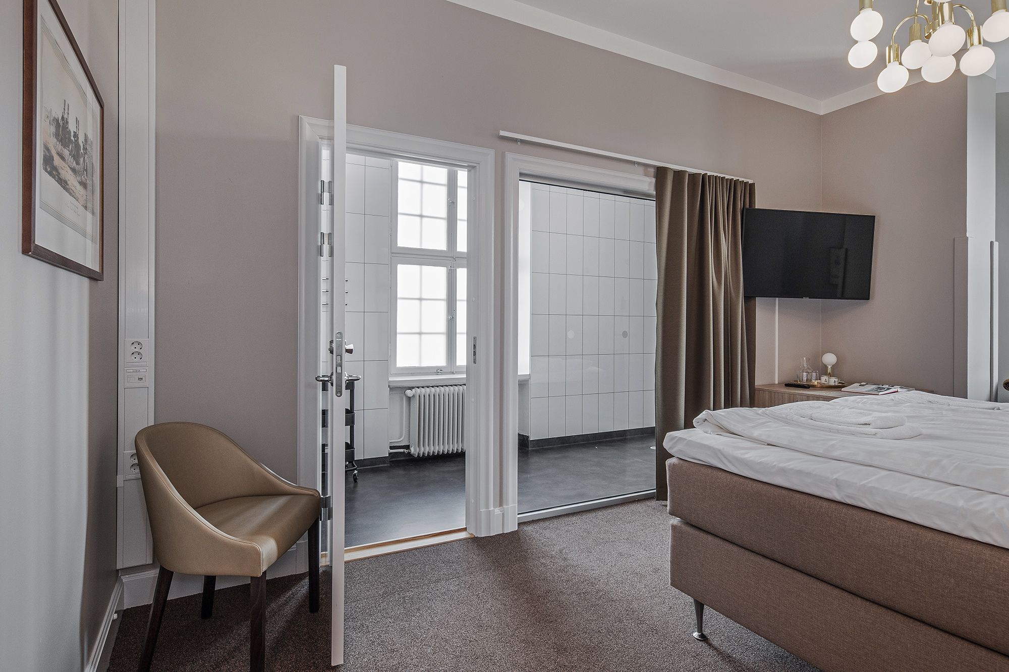 Una habitación de hotel con una cama, una silla, un televisor y una puerta que da a un baño.