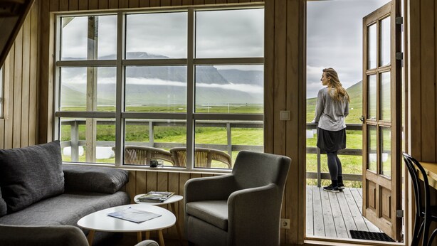 A room with a large window, a sofa, a small table, and a chair. - Korpudalur (Flateyri)