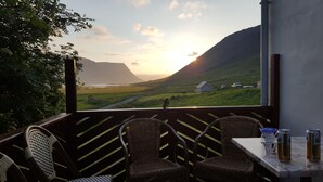 A balcony with wicker chairs, a table with drinks, and a scenic view of a coastal landscape with houses and mountains. - Korpudalur (Flateyri)