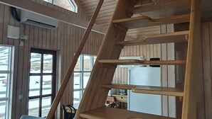 A wooden staircase with a handrail, leading to a second-floor area with a window and a chair. - Korpudalur (Flateyri)