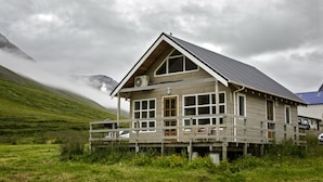 A wooden cabin with a balcony, surrounded by a grassy landscape and mountains. - Korpudalur (Flateyri)