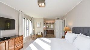 A hotel room with a large bed, a television on a wooden dresser, a small table with a lamp, and a view of the kitchen and bathroom through an open door. - 305 Northgate at Silverado in Napa - One Bedroom Condo (Napa)
