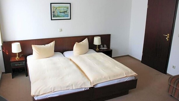 A hotel room with a double bed, two bedside lamps, a nightstand, a framed picture on the wall, and a door.
