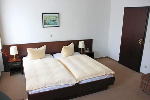 Une chambre d’hôtel avec un lit double, deux lampes de chevet, une table de chevet, un tableau encadré au mur et une porte.