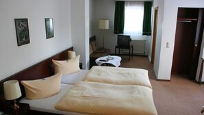 A hotel room with a double bed, bedside tables, a desk with a chair, a television, and a window with curtains.