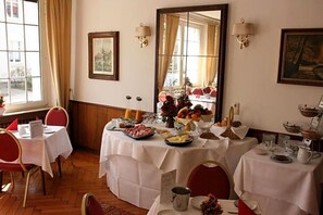 Un coin repas avec des tables préparées pour le petit-déjeuner, où l’on trouve une variété d’aliments et un miroir qui reflète la pièce.