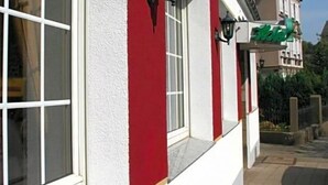 A building with a red and white facade, large windows, and a green sign indicating a hotel.