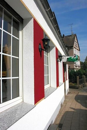 Un bâtiment à la façade rouge et blanche, doté de grandes fenêtres et d’une enseigne verte indiquant qu’il s’agit d’un hôtel.