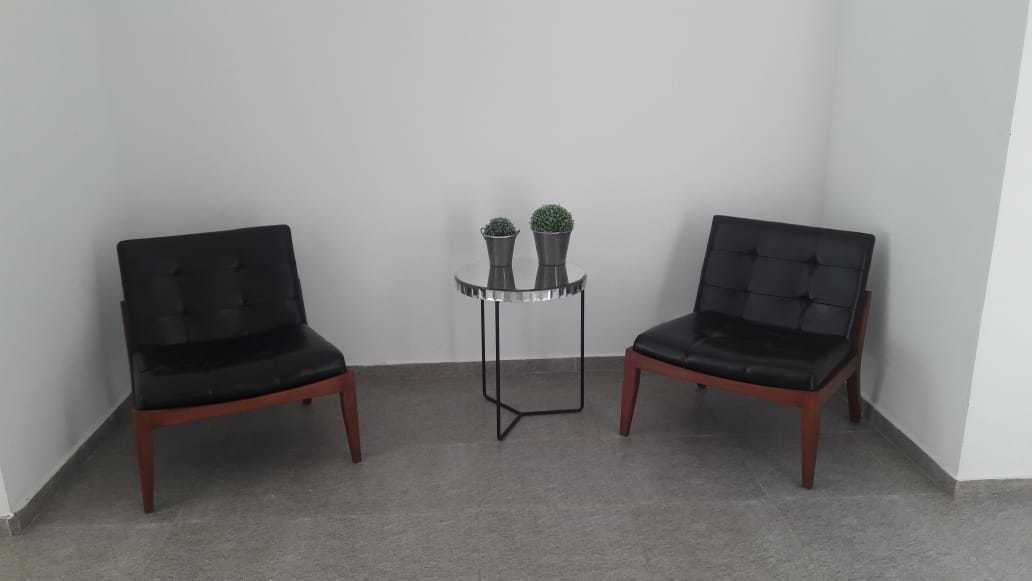 Two black upholstered chairs with wooden legs, a small round table with a metal frame, and two potted plants on the table.