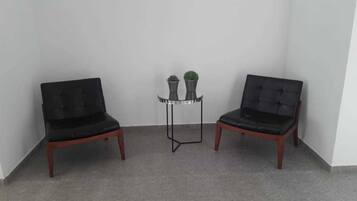 Two black upholstered chairs with wooden legs, a small round table with a metal frame, and two potted plants on the table.