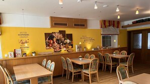 A restaurant interior with wooden tables and chairs, a yellow wall with text and a fruit display, and pendant lighting.
