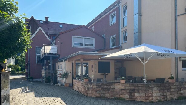 A courtyard with a brick pathway, outdoor seating, and a building with a red facade and a beige section.