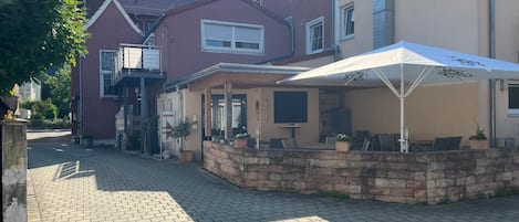 Un patio con sendero de ladrillo, mobiliario exterior y un edificio con fachada roja y sección color beige.