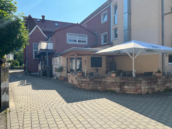 A courtyard with a brick pathway, outdoor seating, and a building with a red facade and a beige section.
