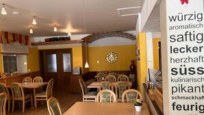 A restaurant interior with wooden tables and chairs, pendant lighting, and a wall clock.