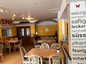 A restaurant interior with wooden tables and chairs, pendant lighting, and a wall clock.