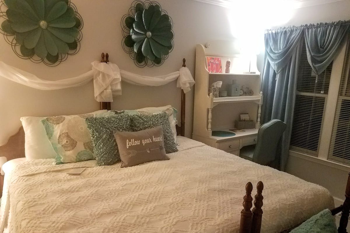 A neatly arranged bedroom with a bed, a bedside table, a chair, and decorative wall art.
