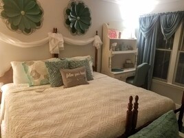 Un dormitorio ordenado con cama, mesita de noche, silla y decoración en la pared.