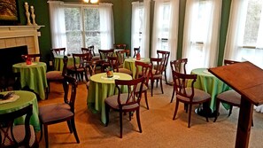 A dining area with round tables covered in green tablecloths, wooden chairs, and a fireplace. - Stockbridge Lakes Bed & Breakfast (Stockbridge)