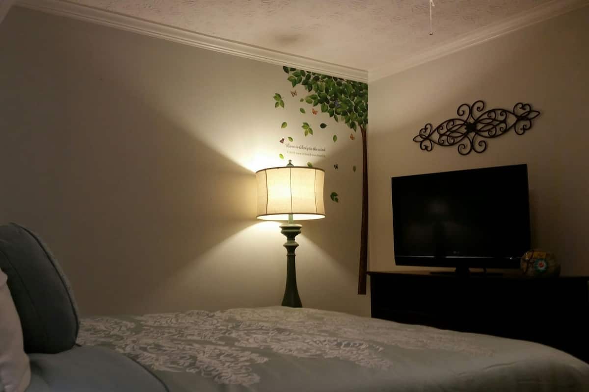 A bedroom with a bed, a lamp, a television, and a wall decoration.