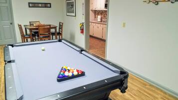 Una mesa de billar con bolas, un comedor con sillas y una cocina visible a través de un vano abierto.