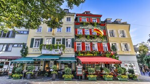 Un café con terraza, un cartel que dice 'Cafe am Rathaus' y un toldo rojo.