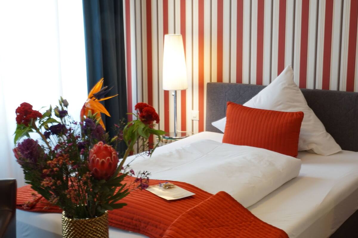 A hotel room with a bed, a vase of flowers, and a lamp.