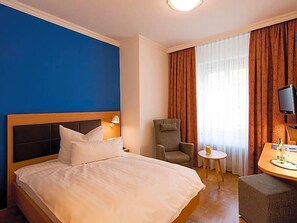 Habitación de hotel con cama, una silla, una mesita con una bebida y un televisor.