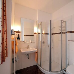 Un baño moderno con cabina de ducha de vidrio, un lavamanos con espejo y un inodoro.