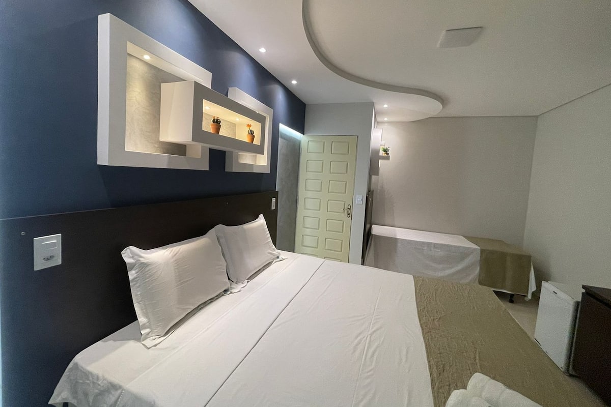 A modern hotel room with a large bed, a built-in shelf with decorative items, a door, and a small table with a white tablecloth.