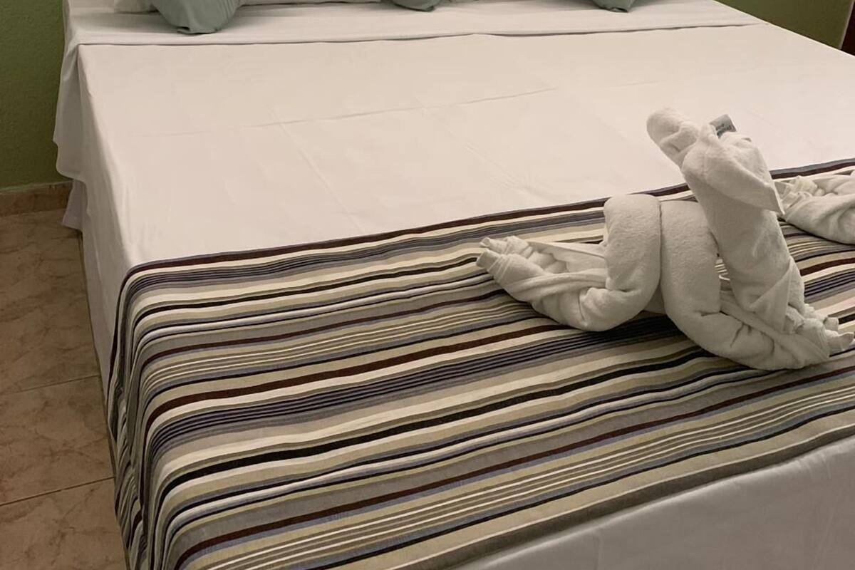 A neatly made bed with a striped bedspread and multiple pillows, including a white towel folded on the bed.