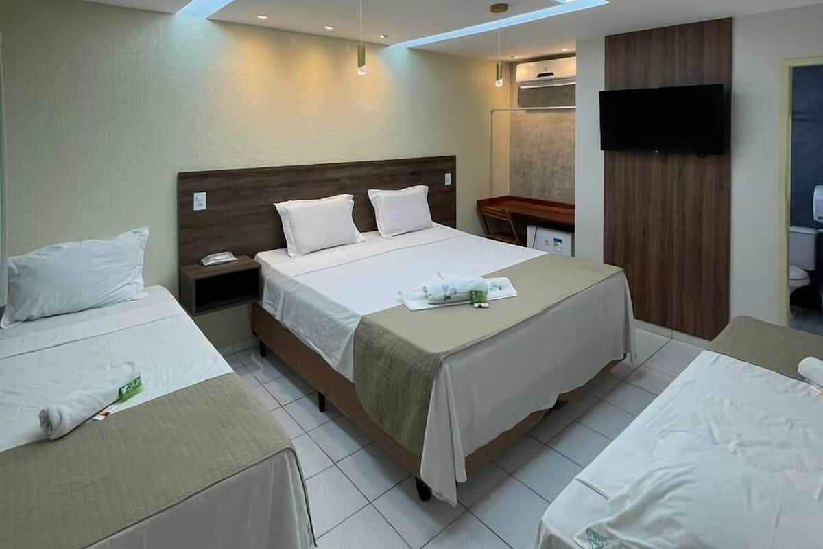 A hotel room with a large bed, two smaller beds, a flat-screen TV, a wooden headboard, and a skylight.