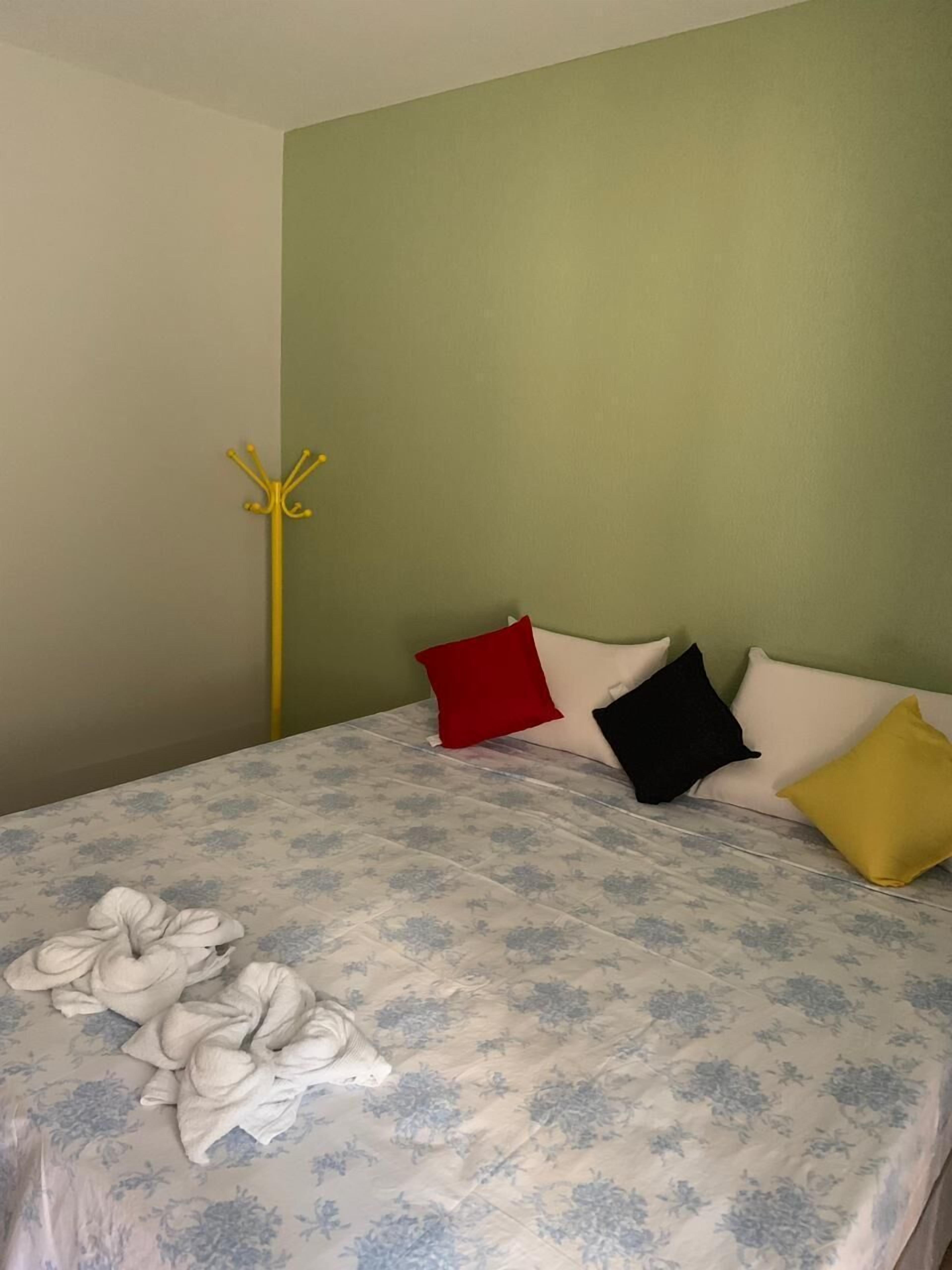A bed with a floral bedspread, a yellow coat rack, and four pillows in red, black, white, and yellow.