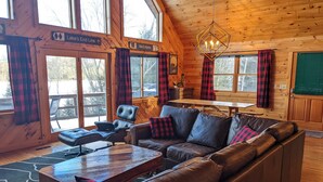 Een gezellig chaletinterieur met een leren bank, een houten eettafel en geruite gordijnen.