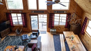 Een gezellig interieur van een vakantiehuisje met een houten vloer, een bank, een eettafel en een plafondventilator.