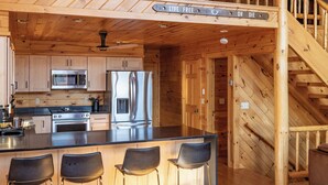 A wooden cabin interior with a kitchen, bar area, and a staircase. - The Lake's End - Beautiful Lakefront Log Home in the White Mountains (Haverhill)
