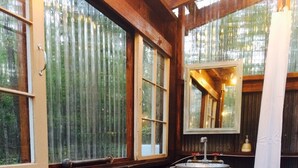 Una habitación acogedora con estufa de leña, un barril grande y una ventana con vistas a árboles.