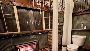A rustic bathroom with a wood-paneled wall, a stone fireplace, a toilet, and a shower curtain.