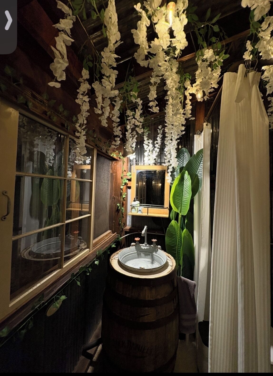Un baño con un lavabo de barril de madera, un espejo y flores blancas colgantes.