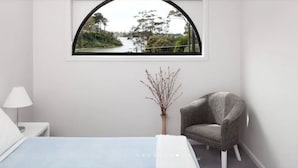 Une chambre à coucher avec un lit, une chaise, une fenêtre donnant sur une rivière et un tableau encadré accroché au mur.