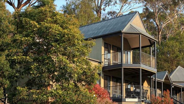 Une maison à deux étages avec un balcon au dernier étage, entourée d’arbres.