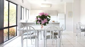 Une cuisine moderne avec des meubles blancs, un plan de travail blanc et un coin repas comprenant une table et des chaises blanches.