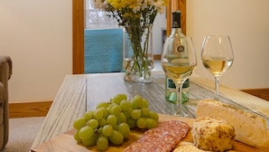 A table with a bottle of white wine, two glasses, a cheese, a salami, and a bunch of grapes.