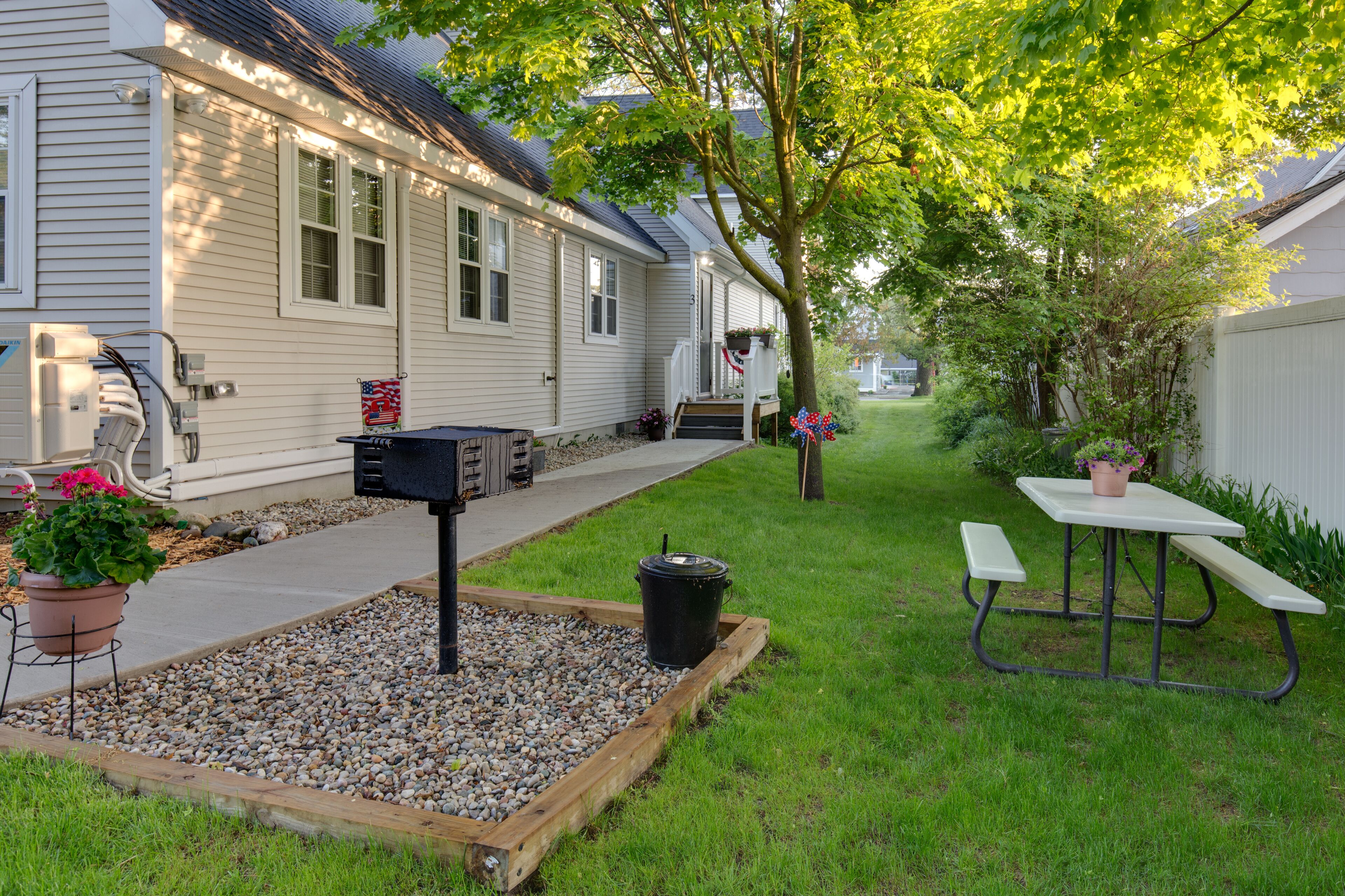A residential setting with a house, a gravel area with a bench, and a picnic table.