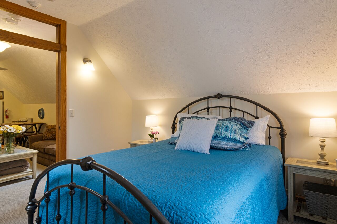 A bedroom with a bed, two bedside tables, a nightstand, a mirror, and a chair.