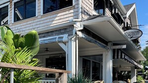 A waterfront property with a covered outdoor seating area, a sign reading "Waterside Market," and a wooden deck with potted plants. - Your Summer Home - Close to Beach, Shops, Cafes, & Ferry! 50+ ⭐️⭐️⭐️⭐️⭐️ Reviews (Vineyard Haven)