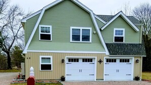 A two-story house with a green siding exterior, two garage doors, and a red mailbox. - Beautifully Renovated, Central AC, wash/dryer, dishwasher, New Appliances. (Charlestown)